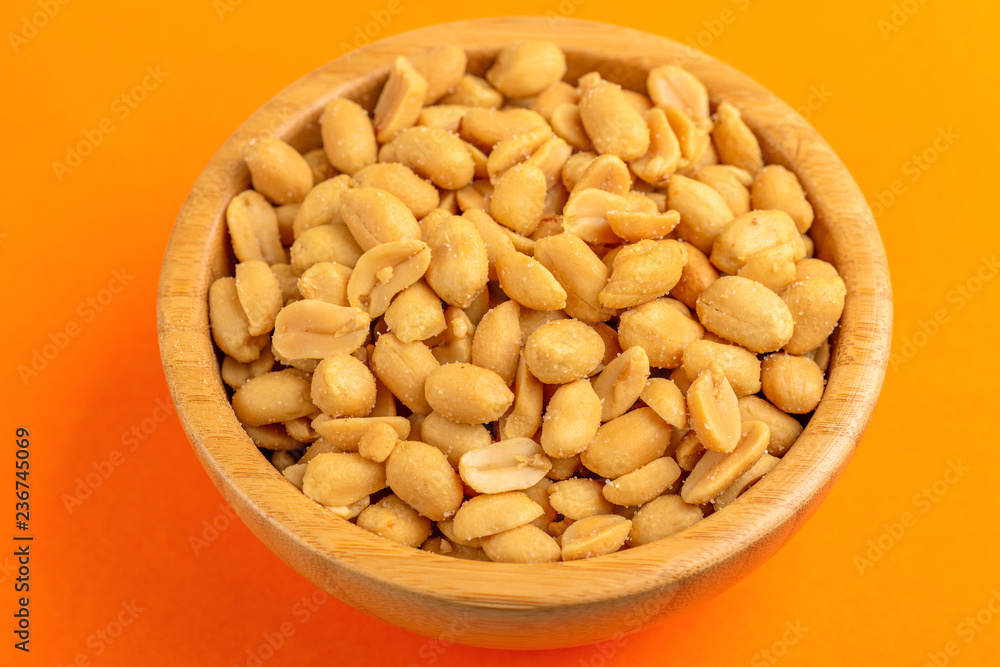 Roasted peanuts in wooden bowl on bright orange background Roasted peanuts in wooden bowl on bright orange background
