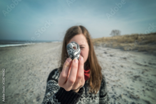 Frau sammelt am Strand Steine und zeigt einen Stein in die Kamera