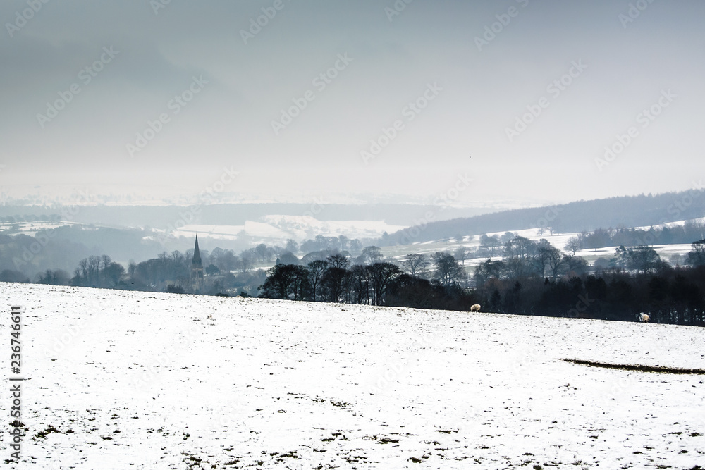 snow landscape in peak district with church spire and rolling hills