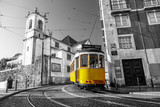 Black and white picture of a yellow tram on the streets of Lisbon, Alfama, Portugal near Santa Luzia church