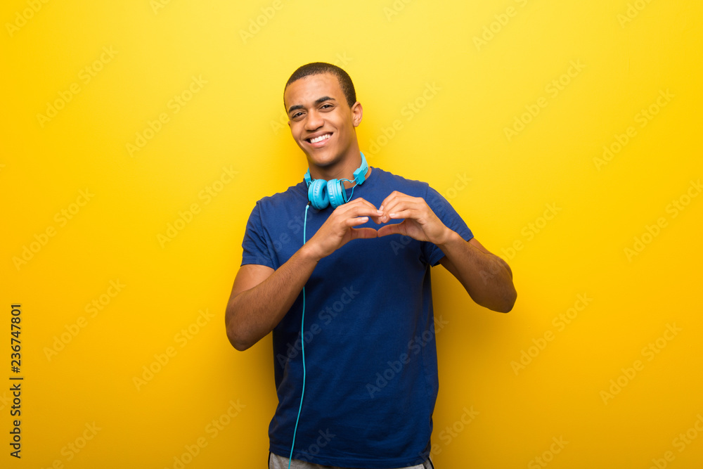 African american man with blue t-shirt on yellow background making heart symbol by hands African american man with blue t-shirt on yellow background making heart symbol by hands