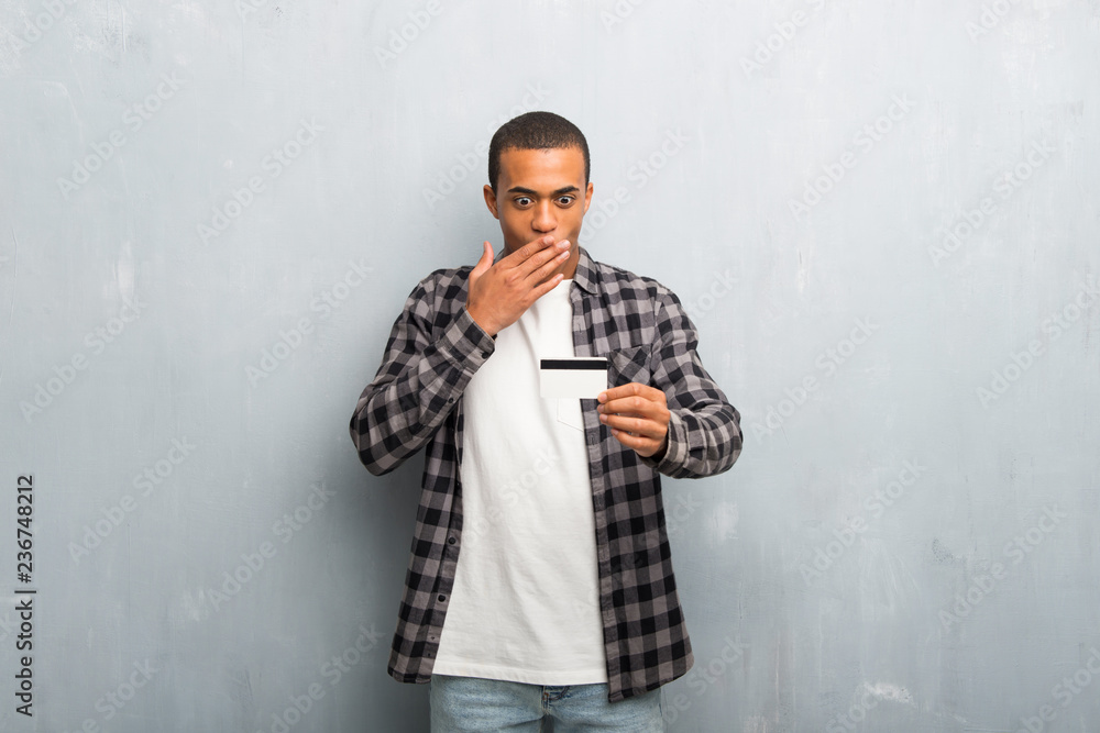 Young african american man with checkered shirt holding a credit card and surprised