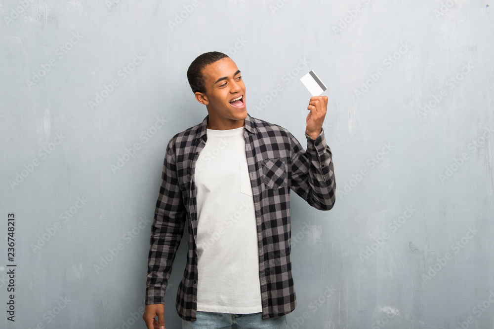 Young african american man with checkered shirt holding a credit card and thinking Young african american man with checkered shirt holding a credit card and thinking