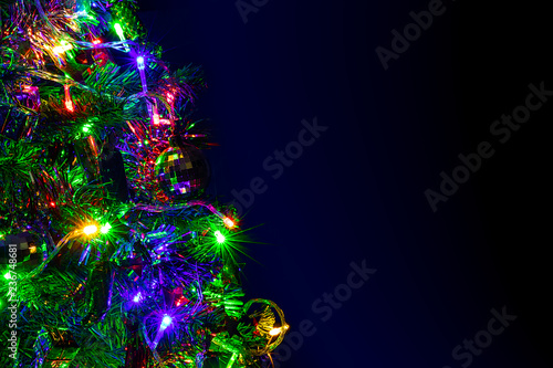 Colored decoration of Christmas tree on dark background. Part of X-mas tree with lighting bulb and decoration at night.
