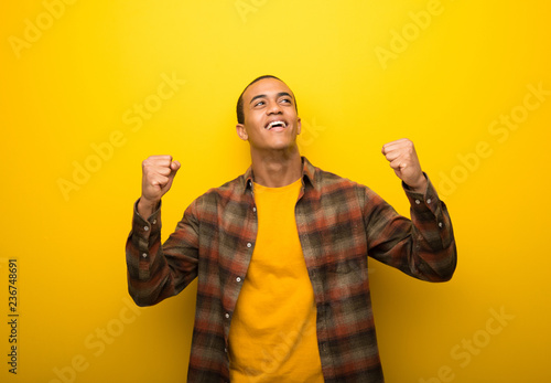 Young african american man on vibrant yellow background celebrating a victory in winner position