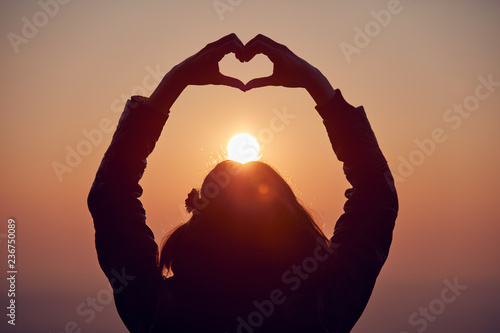 Girl making heart - shape sign with hands at sunset / sunrise time.