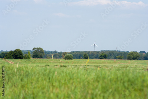 Landscape in Germany, in the foreground green meadows and forest in the background. A windmill generating electricity is visible.