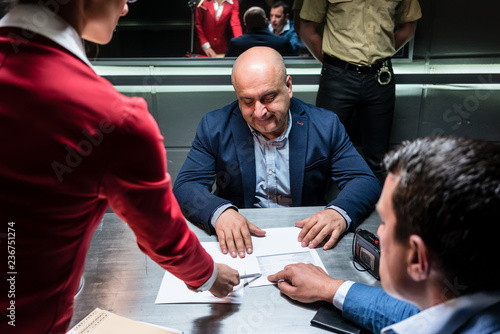 Middle-aged defendant or witness, counseled by the lawyer to sign an official statement in front of the prosecutor during a criminal investigation in the police station