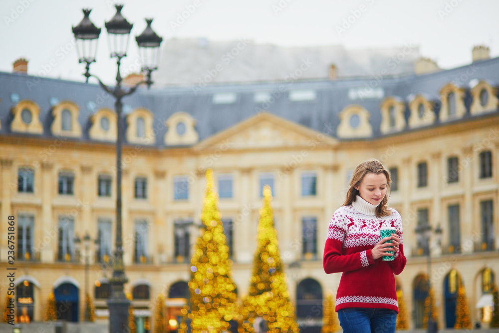 Girl walking with hot drink to go on a street of Paris decorated for Christmas