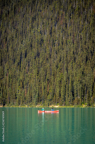 Banff, Canada - Sept 15th 2017 - Couple of tourists doing kayak in a green water lake with pine trees in the background at the Banff National Park in Canada