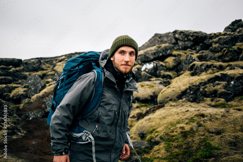 Smiling and happy portrait of young handsome traveller or hiker enjoying the outdoors activity. Wears winter jacket and beanie, together with backpack for tent and gear. Nomad lifestyle Smiling and happy portrait of young handsome traveller or hiker enjoying the outdoors activity. Wears winter jacket and beanie, together with backpack for tent and gear. Nomad lifestyle