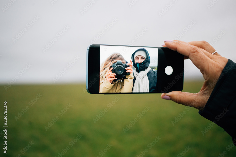 Mother and daughter, young family make selfie on smartphone with big digital screen during hike or adventure camping trip in cold weather. Happy enjoying nature elements. Female vacation