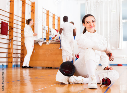 Woman in uniform sitting on floor at fencing training