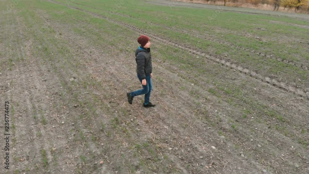 The lonely boy wanders in autumn in an empty, plowed, gray field. The croaker is looking for something in the field. The boy is running and walking. The lonely boy wanders in autumn in an empty, plowed, gray field. The croaker is looking for something in the field. The boy is running and walking.