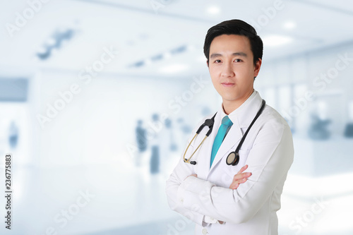 Doctor posing with arms crossed, medical staff working on blurry background.