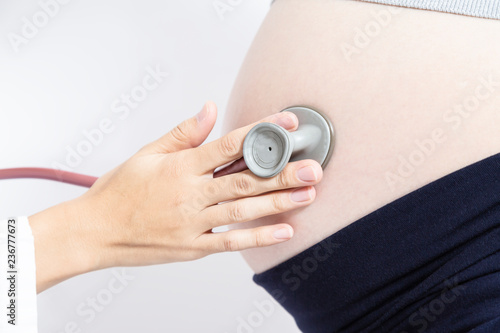 妊婦の大きなお腹を聴診器で診察する女医の手元のアップ。妊娠、診察、臨月、検査,産婦人科、女医イメージ