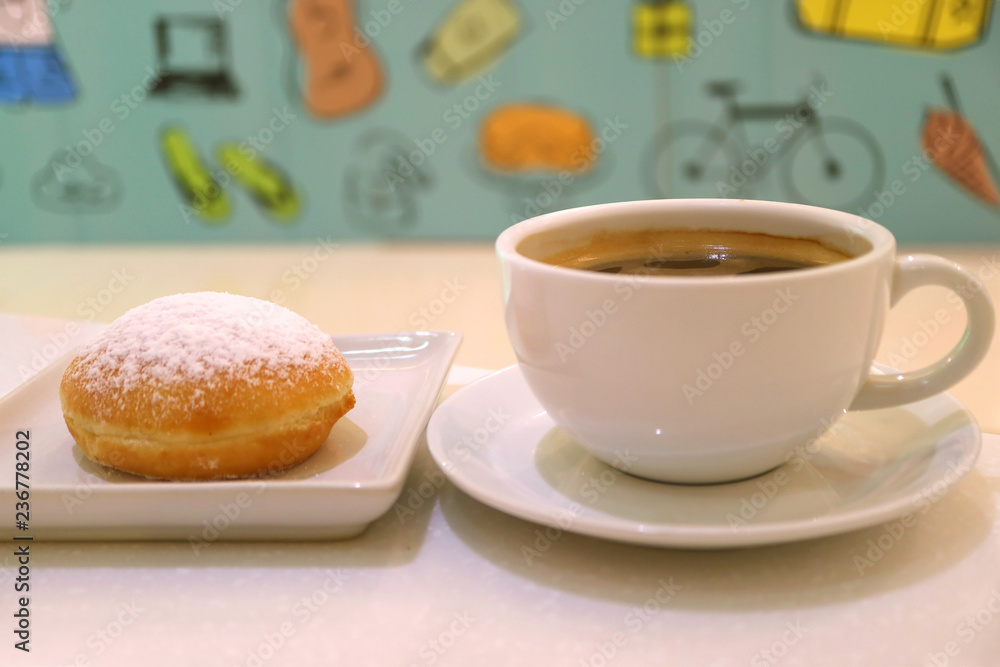 Cup of hot coffee and a strawberry jam filled doughnut with blurred colorful wall paper in background Cup of hot coffee and a strawberry jam filled doughnut with blurred colorful wall paper in background