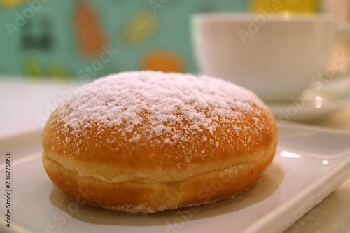 One strawberry jam filled doughnut with blurred white coffee cup in background 