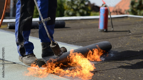 Hand vom Dachdecker Bauarbeiter auf Immobilien Flachdach Haus: Bitumen Dachbahn zuhause auf kaputtes Dach mit offenem Feuer kleben, freier Platz