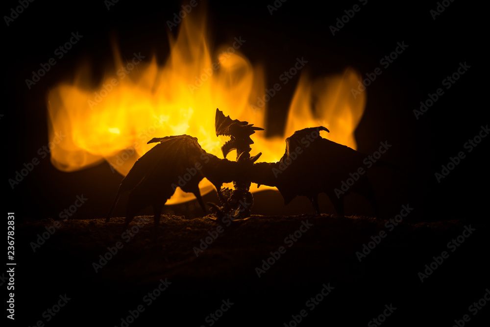Fototapeta premium Silhouette of fire breathing dragon with big wings on a dark orange background