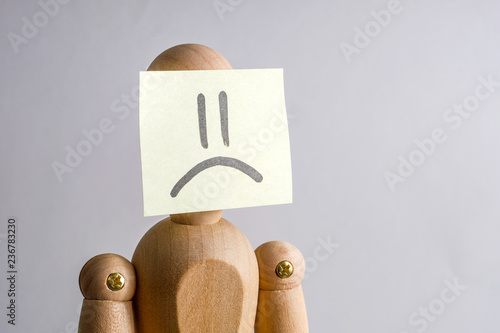 Concept face of an unhappy person. Wooden mannequin with a sticker on his face with the image of sadness. photo