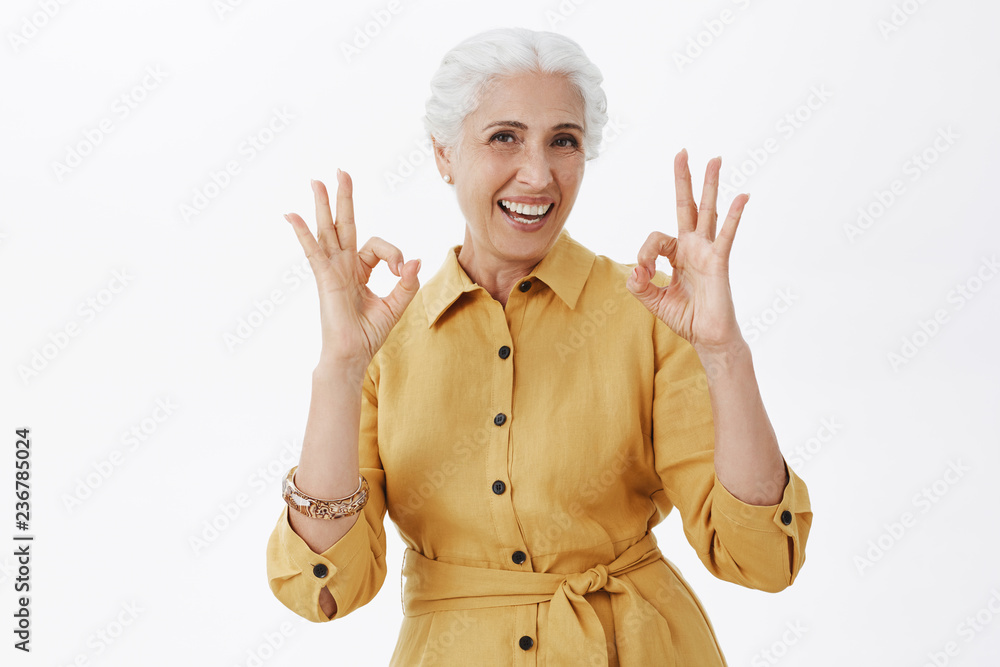 Granny has excellent health. Portrait of joyful active and emotive senior woman with white hair smiling joyfully and laughing showing okay or perfect gesture posing in trendy yellow coat Granny has excellent health. Portrait of joyful active and emotive senior woman with white hair smiling joyfully and laughing showing okay or perfect gesture posing in trendy yellow coat