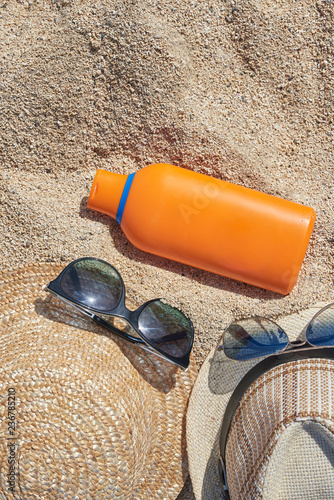 Male and female sunglasses,  sunhats and a sunprotection cream at the sand as a reminder of protection importance during the sun exposure.