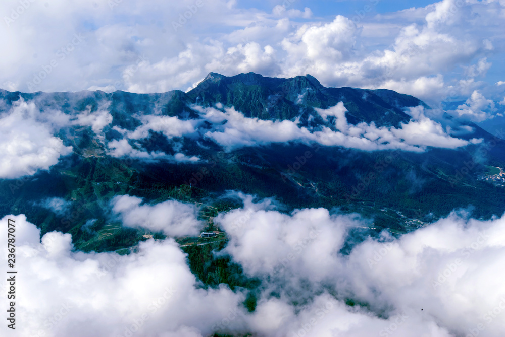 view from above, from the peak or from an airplane, to a wooded mountain valley with settlements, partly hidden by cumulus clouds view from above, from the peak or from an airplane, to a wooded mountain valley with settlements, partly hidden by cumulus clouds