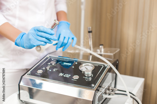 Unrecognizable young doctor with medical equipment. Female cosmetologist with dermatological apparatus of microdermabrasion in latex gloves. Polishing tool background.