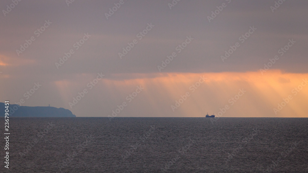 A boat on the horizon in sun rays on a stormy day