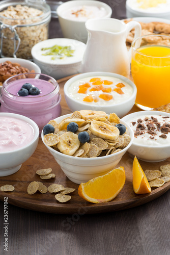 rich breakfast buffet with cereals, yoghurt and fruit on wooden tray, vertical