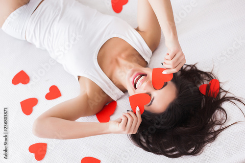 Very beautiful young woman liying on the bed. Top view of attractive girl with paper hearts photo