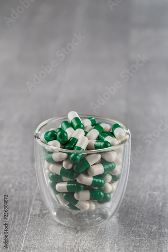 close-up of white-green pills in glass Cup on grey background