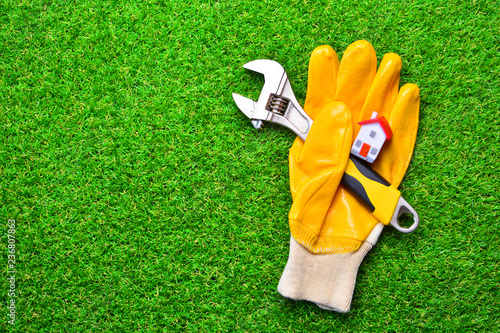 Apartment renovation background. Home repairs concept. Building glove with a adjustable wrench and miniature house on a green grass. Copy space.