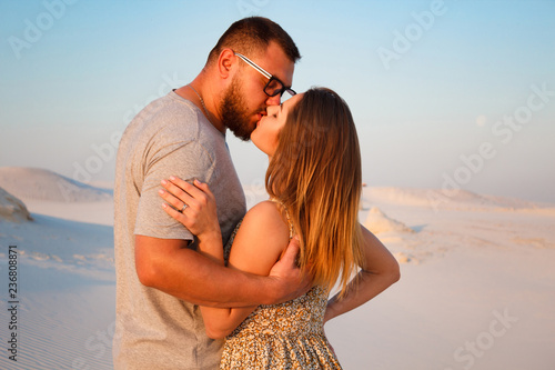 lovely attractive couple kissing on the white sand beach or in the desert or in the sand dunes, happy couple embracing at the beach on a sunny day, couple in love © ig_royal