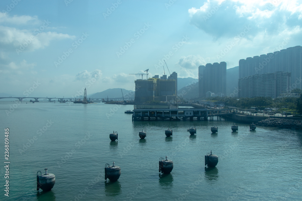 City near the sea. Buoys on the sea, in the distance a large bridge. Construction of a building in Hong Kong.