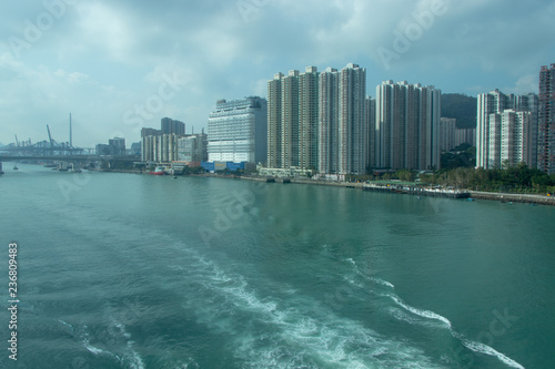 City near the sea. Waves on the water from the boat sailed away, a large bridge in the distance. Tall city buildings.