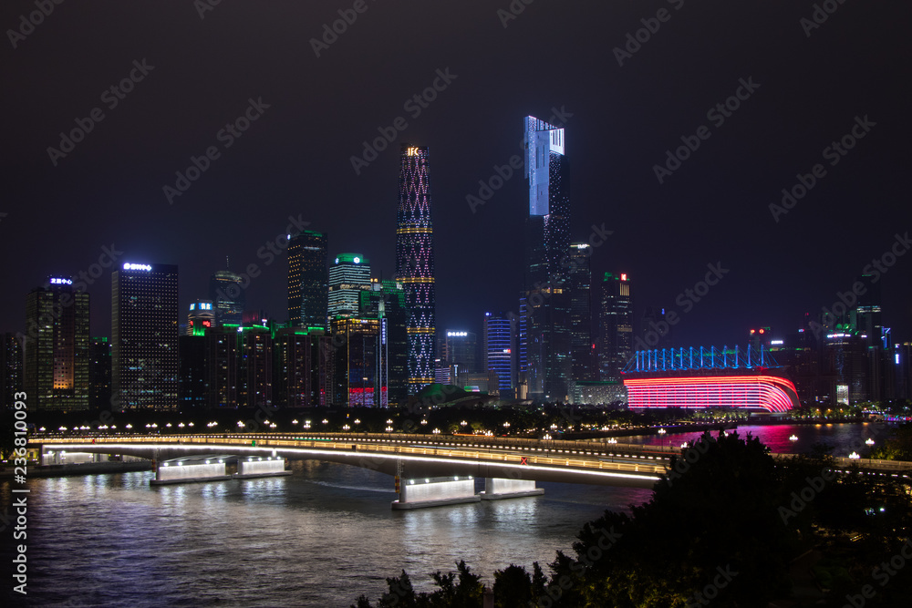 Night modern city with skyscrapers. Bridge over the river, city buildings glow at night. The sky in the clouds hides the building. Travel to China Guangzhou City.