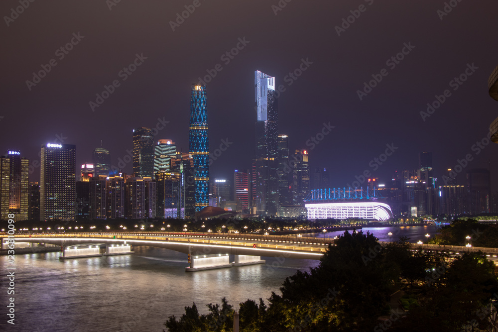 Fototapeta premium Night modern city with skyscrapers. Bridge over the river, city buildings glow at night. The sky in the clouds hides the building. Travel to China Guangzhou City.
