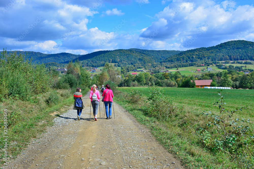 Group of tourist, hikers and backpackers are waling on the country road. Beautiful nature around them. 
Outdoor activity and walking in the countryside. Wysowa, Low Beskids (Beskid Niski), Poland