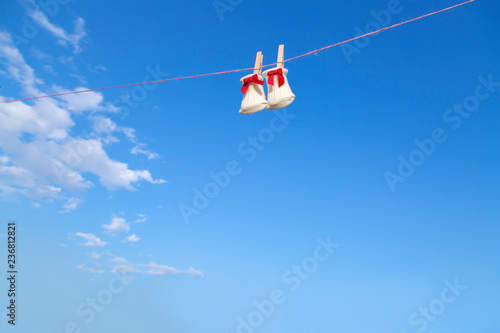 青空に木製洗濯挟みで吊るされた赤いリボンの新生児用靴下。赤ちゃん、育児、出産、幸せ、愛イメージ