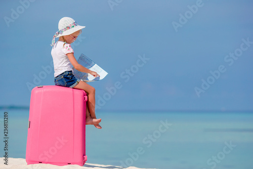 Little tourists girl with big suitcase on tropical white beach