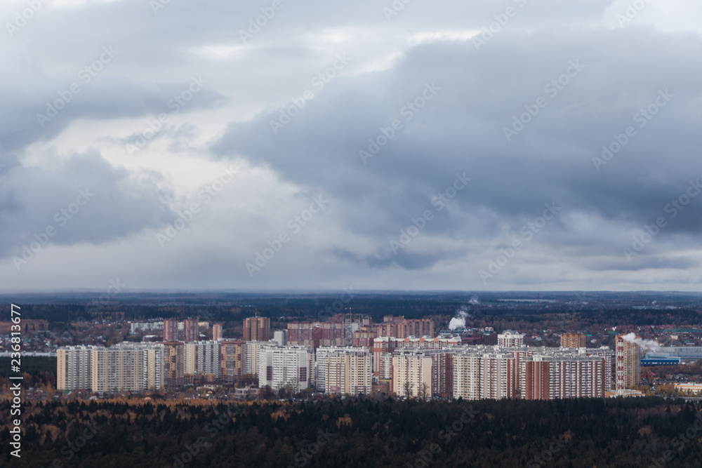 High-rise buildings of the city near the forest. A small city with an altitude of the aircraft. At the top of the white clouds on the horizon, below the forest, city buildings.