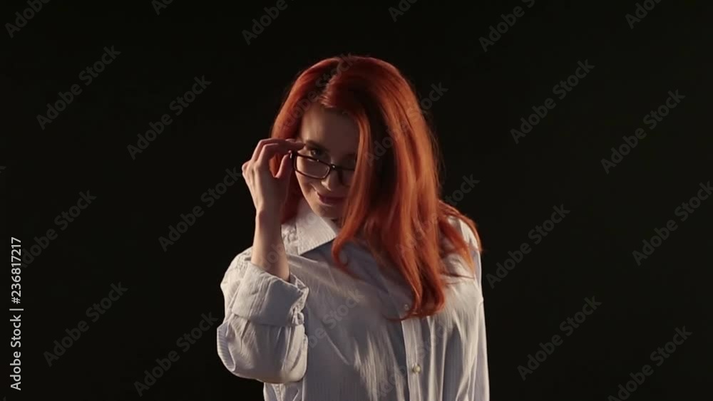 a beautiful girl with red hair in a white shirt posing on a black ...