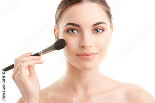 Young naked woman applying makeup. Studio shot.