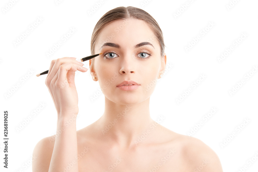 Young naked woman applying makeup. Studio shot.