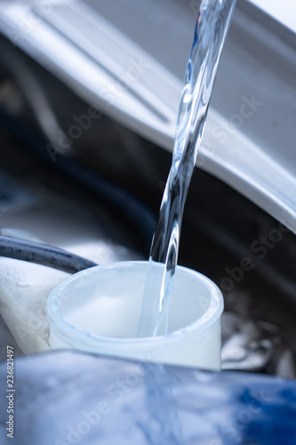 The person pours non-freezing liquid into the tank of the car.