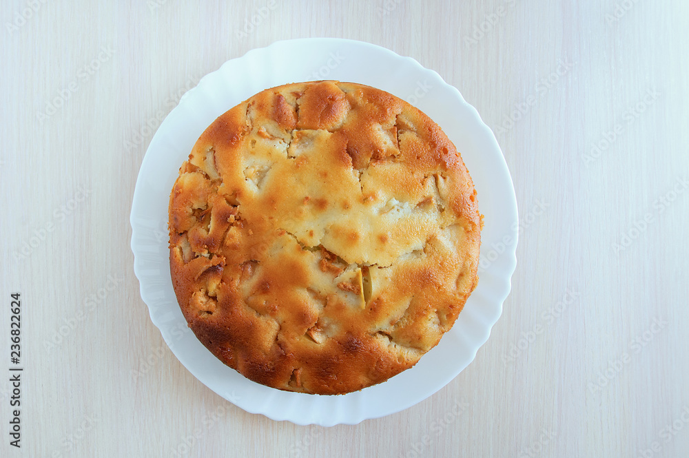 Freshly baked apple pie on a white plate. On a wooden table. View from above. Freshly baked apple pie on a white plate. On a wooden table. View from above.