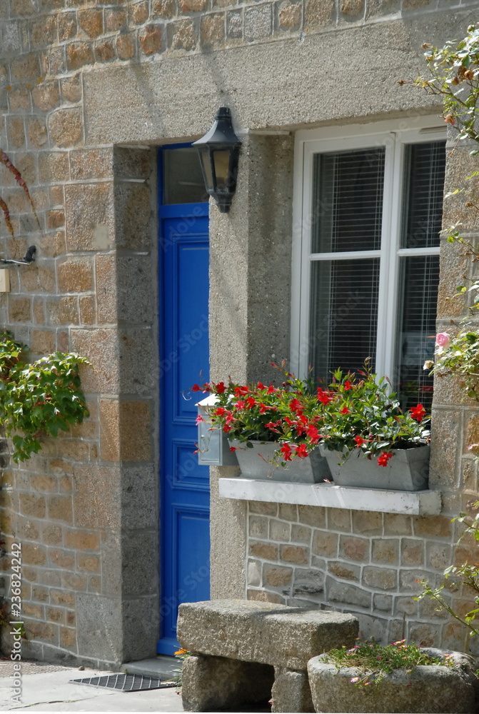 Ville de Genêts, maison en pierre, porte bleue et fleurs au bord de la fenêtre, banc en pierre, département de la Manche, France	