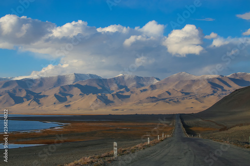 Pamir Highway, the road goes beyond the horizon near a mountain lake